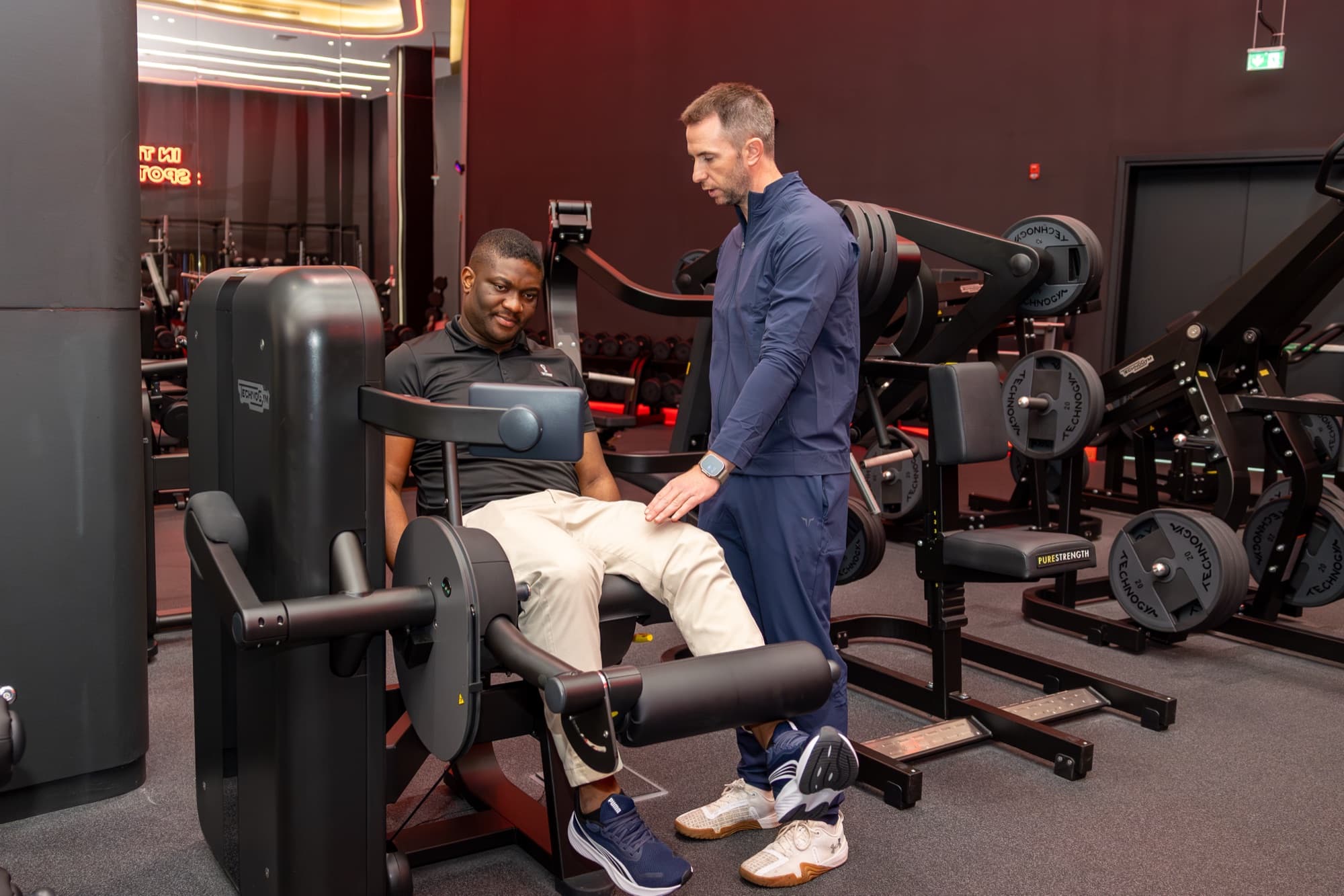 Physiotherapist guiding a patient through a leg extension strengthening exercise in the gym at Virgin Active Msheireb, Doha